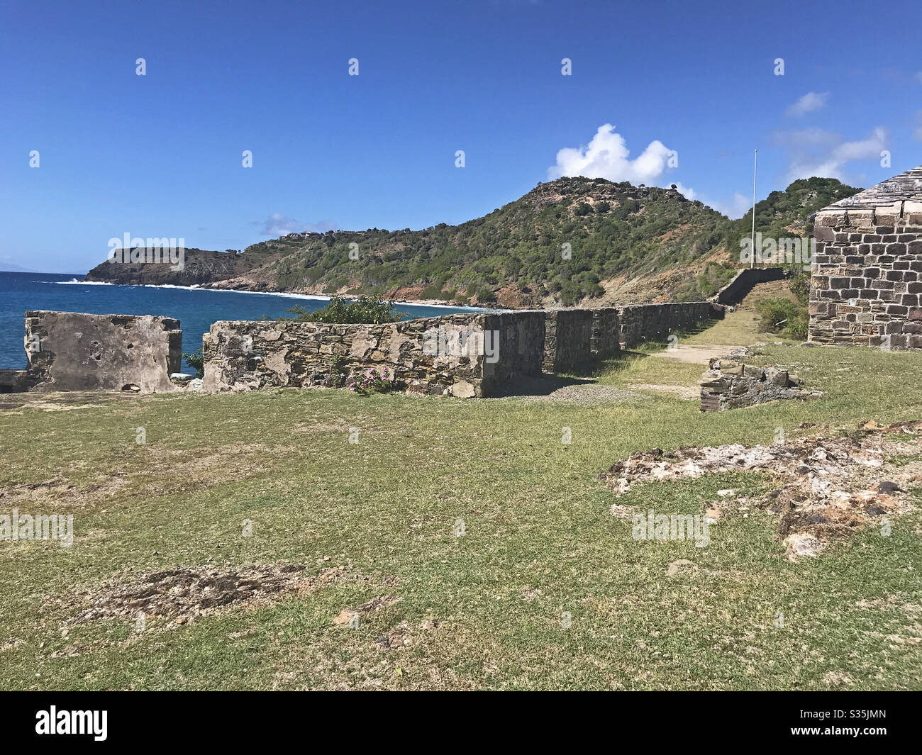 Antigua coastline, Guard House and outer fort wall with cannon ports as seen from the Fort Berkeley Peninsula in Antigua and Barbuda, Caribbean, Lesser Antilles, West Indies with blue sky copy space. - Smartphone Captured Stock Image