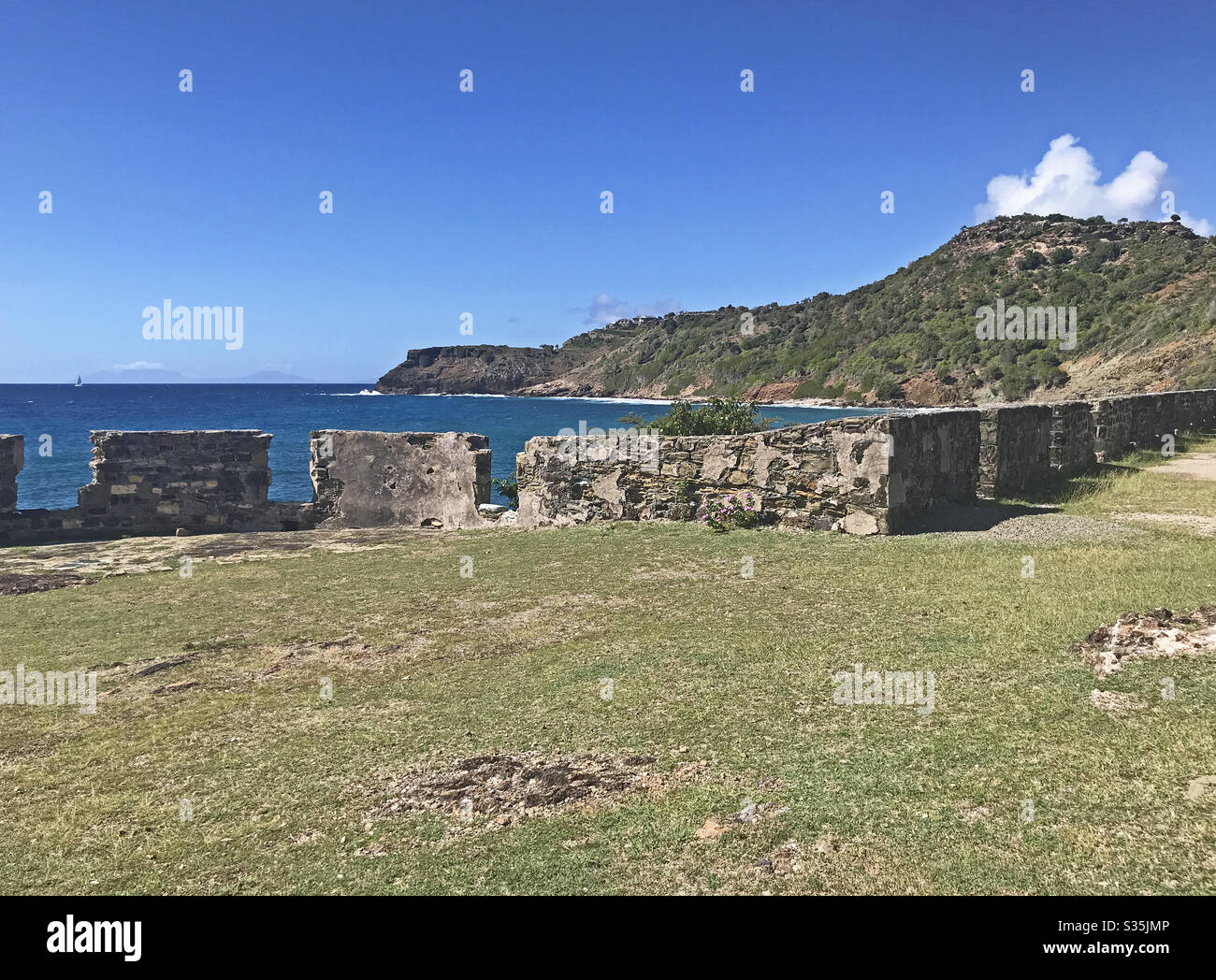 Antigua coastline and outer fort wall with cannon ports as seen from the Fort Berkeley Peninsula in Antigua and Barbuda, Caribbean, Lesser Antilles, West Indies with blue sky copy space. - Smartphone Captured Stock Image