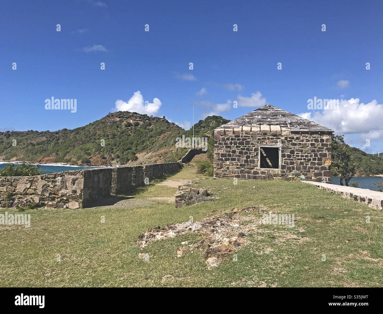 Antigua coastline, Guard House and outer fort wall with cannon ports as seen from the Fort Berkeley Peninsula in Antigua and Barbuda, Caribbean, Lesser Antilles, West Indies with blue sky copy space. - Smartphone Captured Stock Image