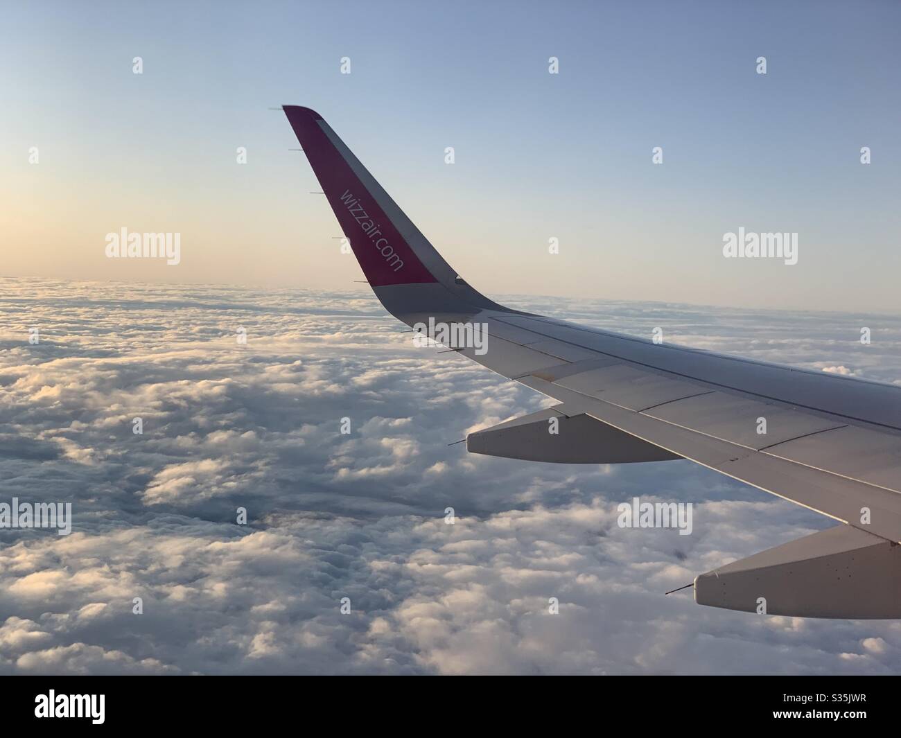 Wizz Air: Wing Tip of a Wizz Air Aircraft above a blanket of clouds in the glow of the setting sun in the background. - Smartphone Captured Stock Image