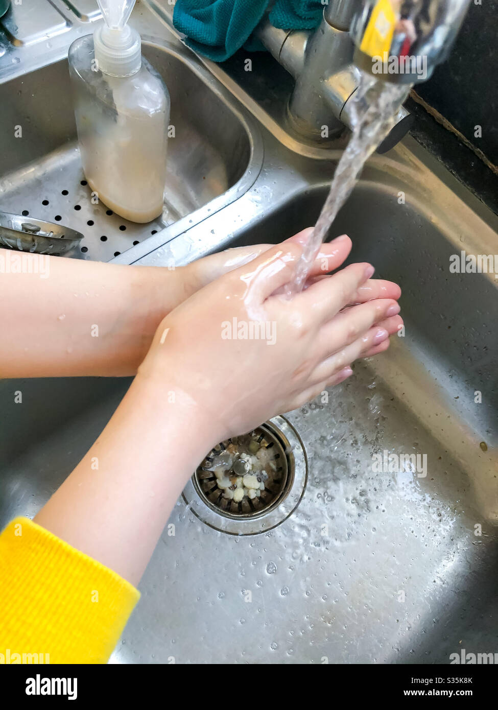 A child washing their hands in the kitchen sink. - Smartphone Captured Stock Image