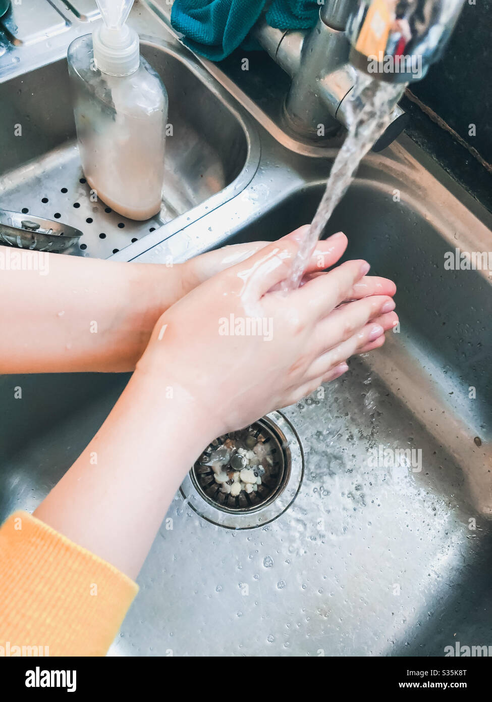 A child washing their hands in the kitchen sink. - Smartphone Captured Stock Image
