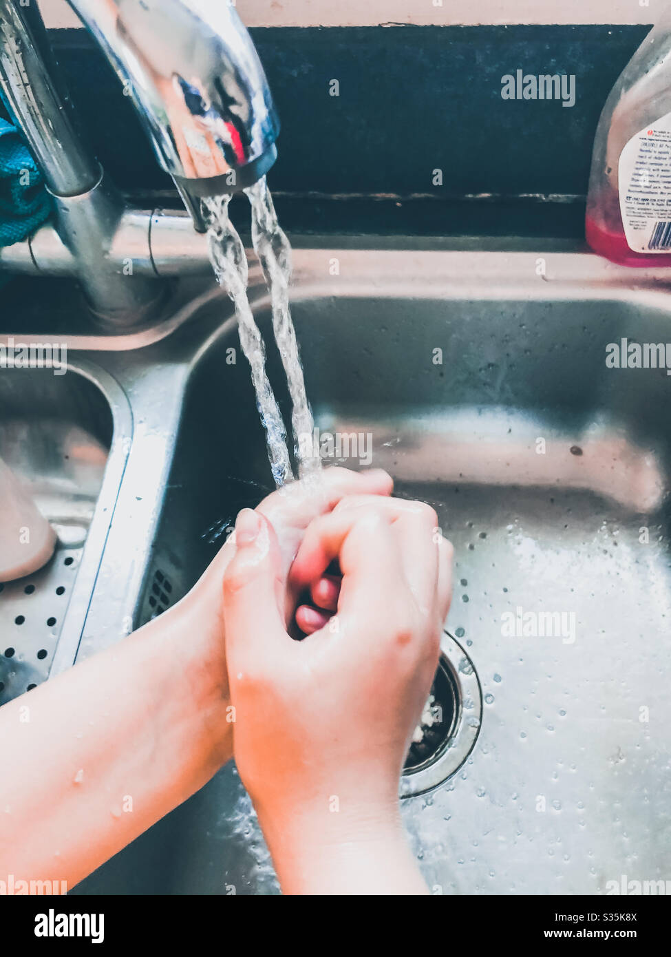 A child washing their hands in the kitchen sink. - Smartphone Captured Stock Image