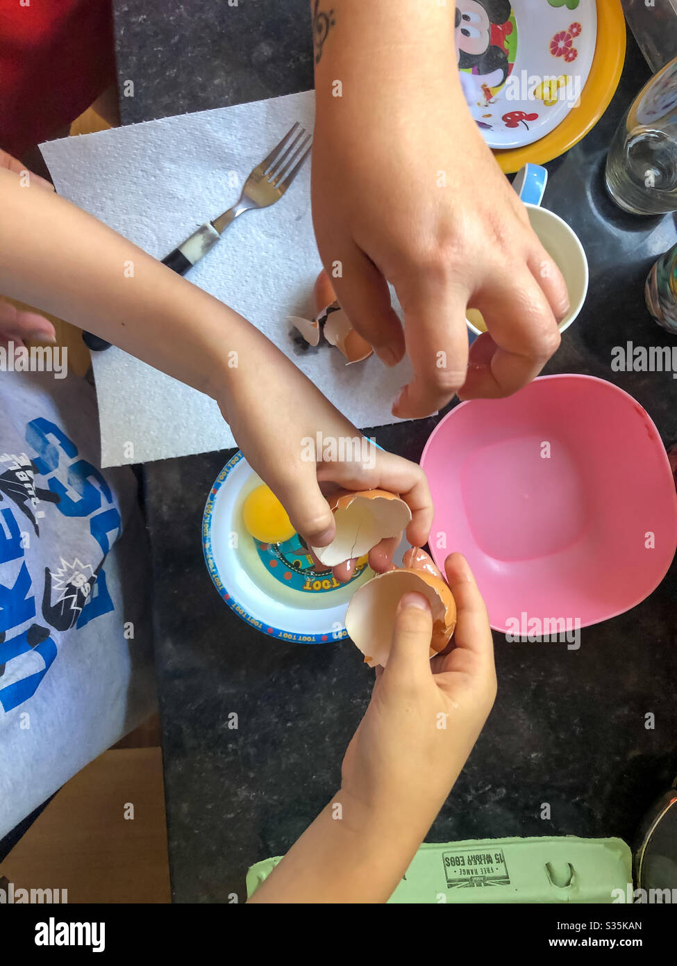 Mother and son cracking an egg into a plastic bowl, seen from above. - Smartphone Captured Stock Image