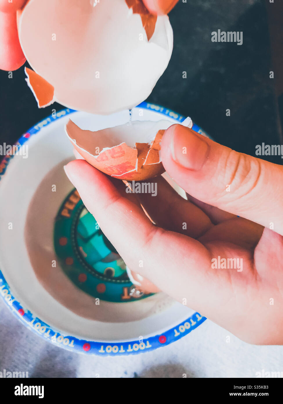 A child cracking eggs into a plastic bowl. - Smartphone Captured Stock Image