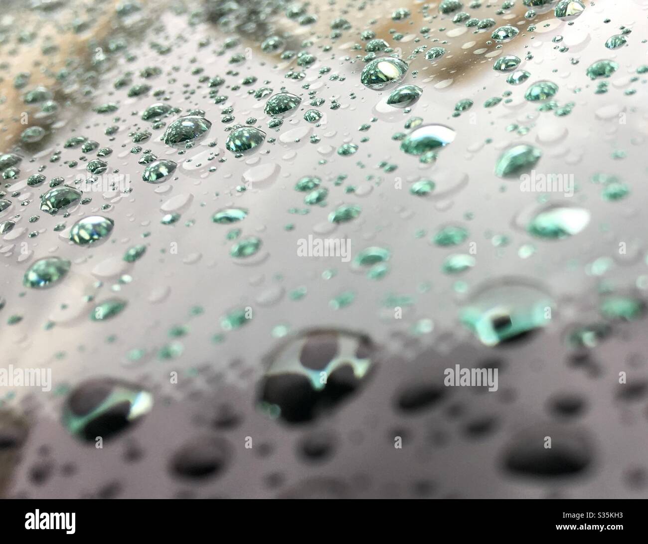 Raindrops, various sizes, light altering colors, shades, side view angle, across windshield, reflection, closeup, weather, nature, natural Stock Photo