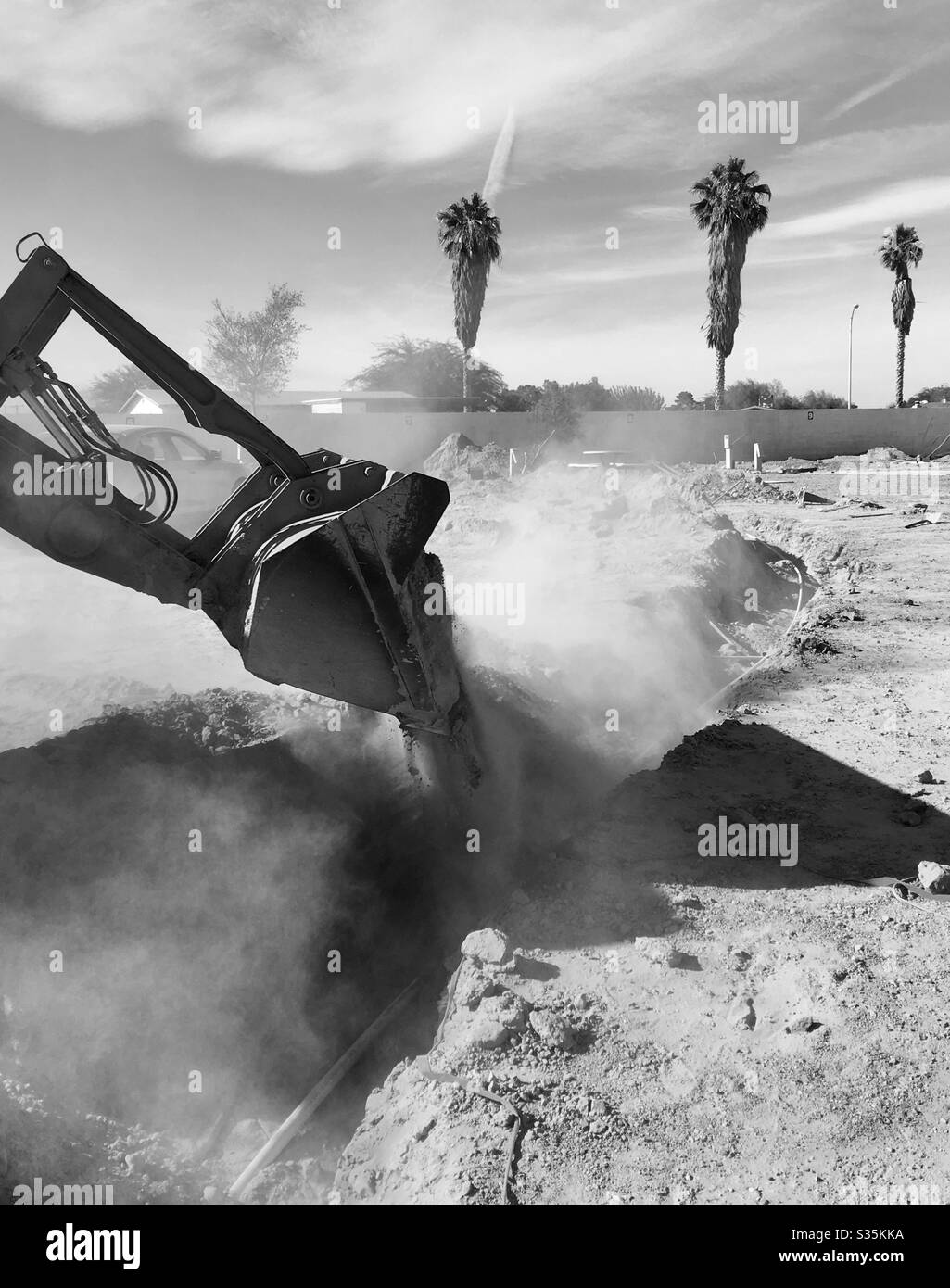 Black white, back home, digging ditch, replacing wiring, RV parking lot, dust in air, desert dirt, background, brick wall, palm trees, blue sky, clouds, copy space, equipment, maintenance, repairs Stock Photo