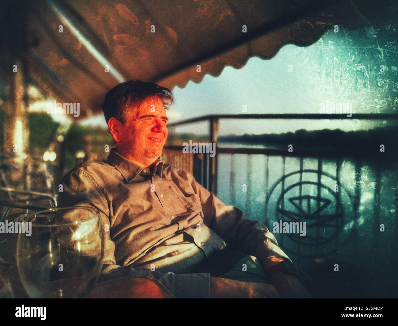 Man enjoying the sunset on the river on a terrace drinking prosecco wine - Smartphone Captured Stock Image