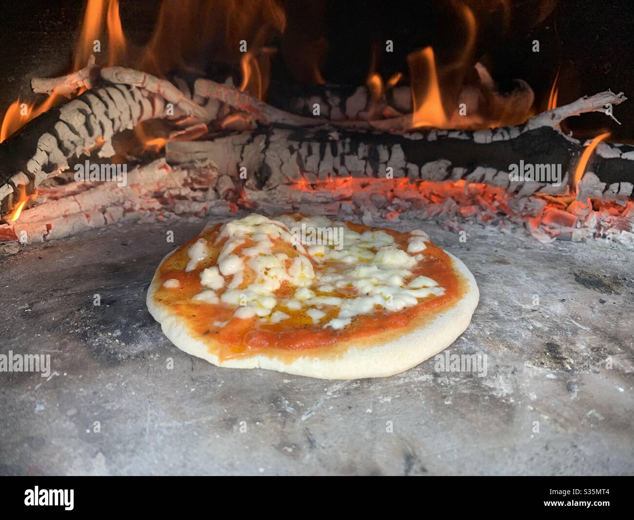 Fresh pizza in a hot pizza oven surrounded by flames and burning wood. Raw pizza. - Smartphone Captured Stock Image