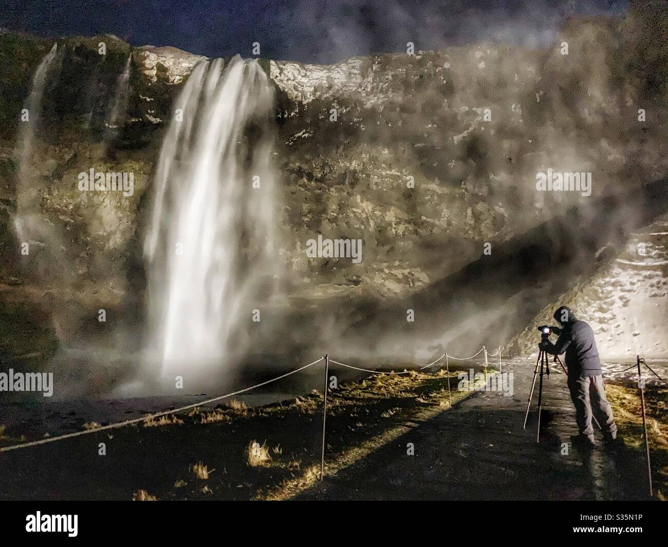 Waterfall Night Photographer. A photographer shoots Seljalandsfoss Waterfall after dark. - Smartphone Captured Stock Image