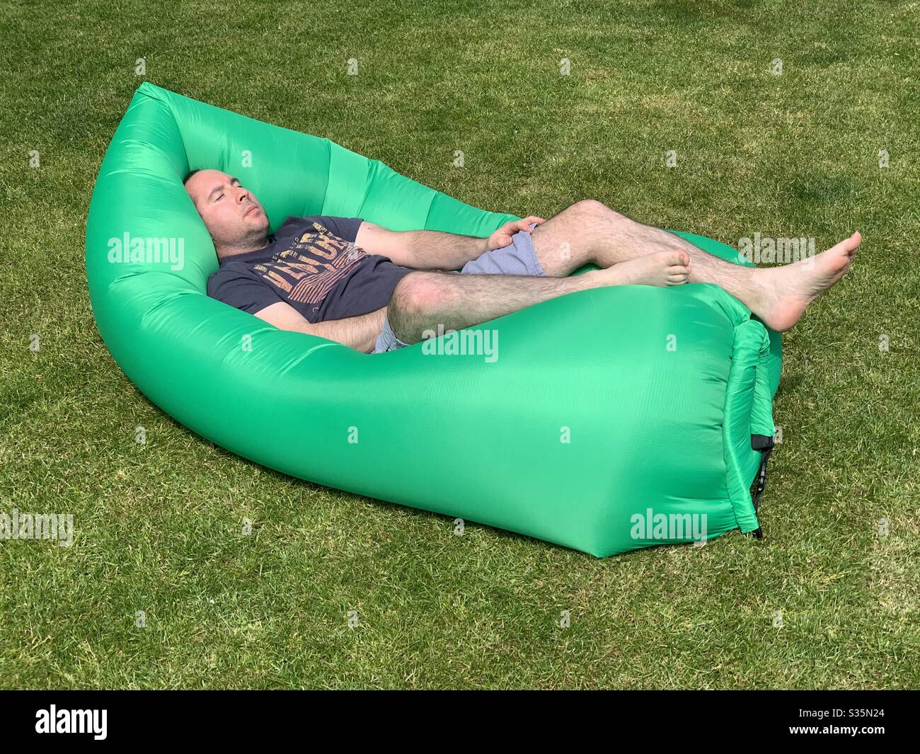 Man sleeps on a large green air bag in the garden. Stock Photo
