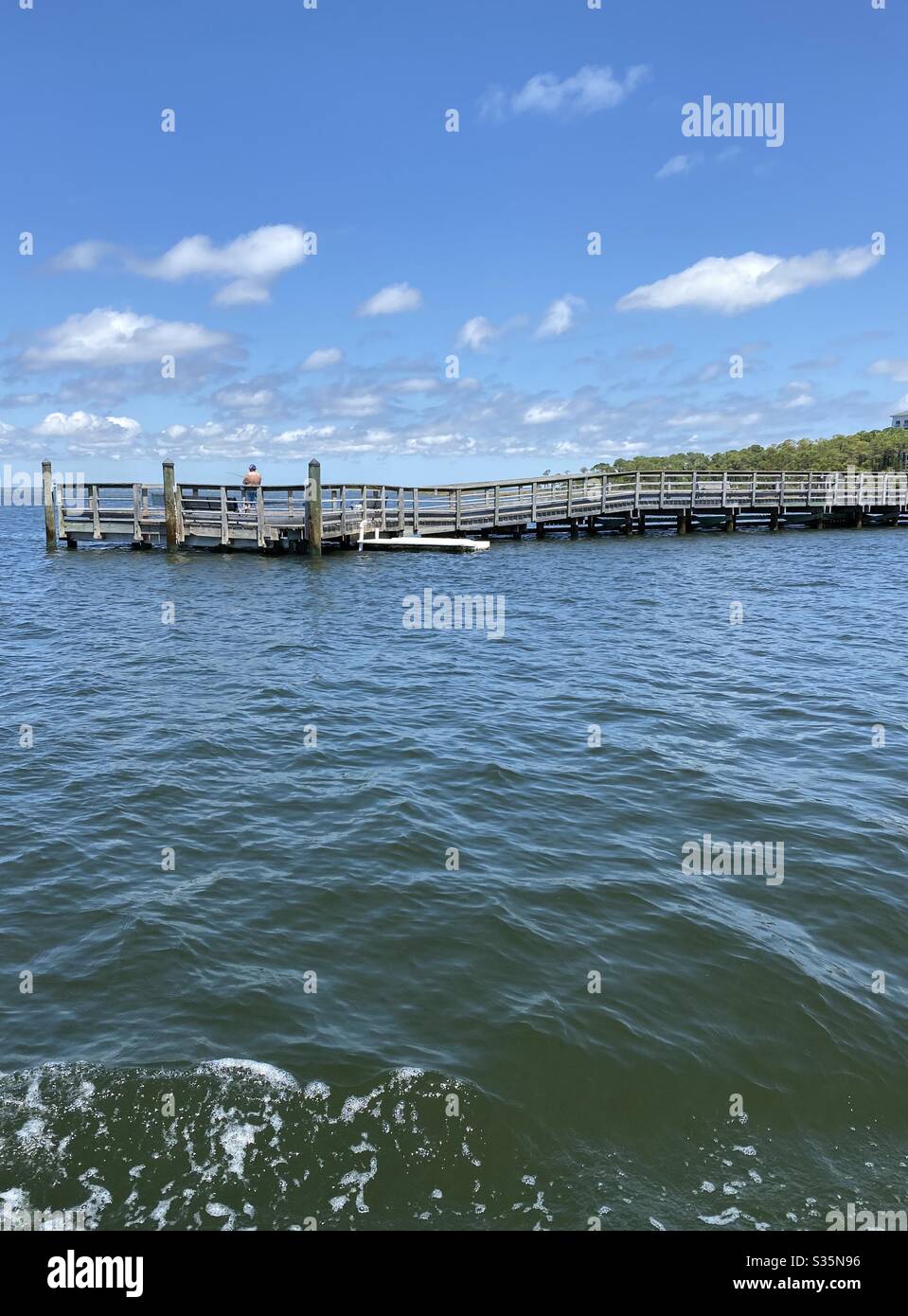 Long wooden pier over the gulf of Mexico water with a fisherman on the pier - Smartphone Captured Stock Image