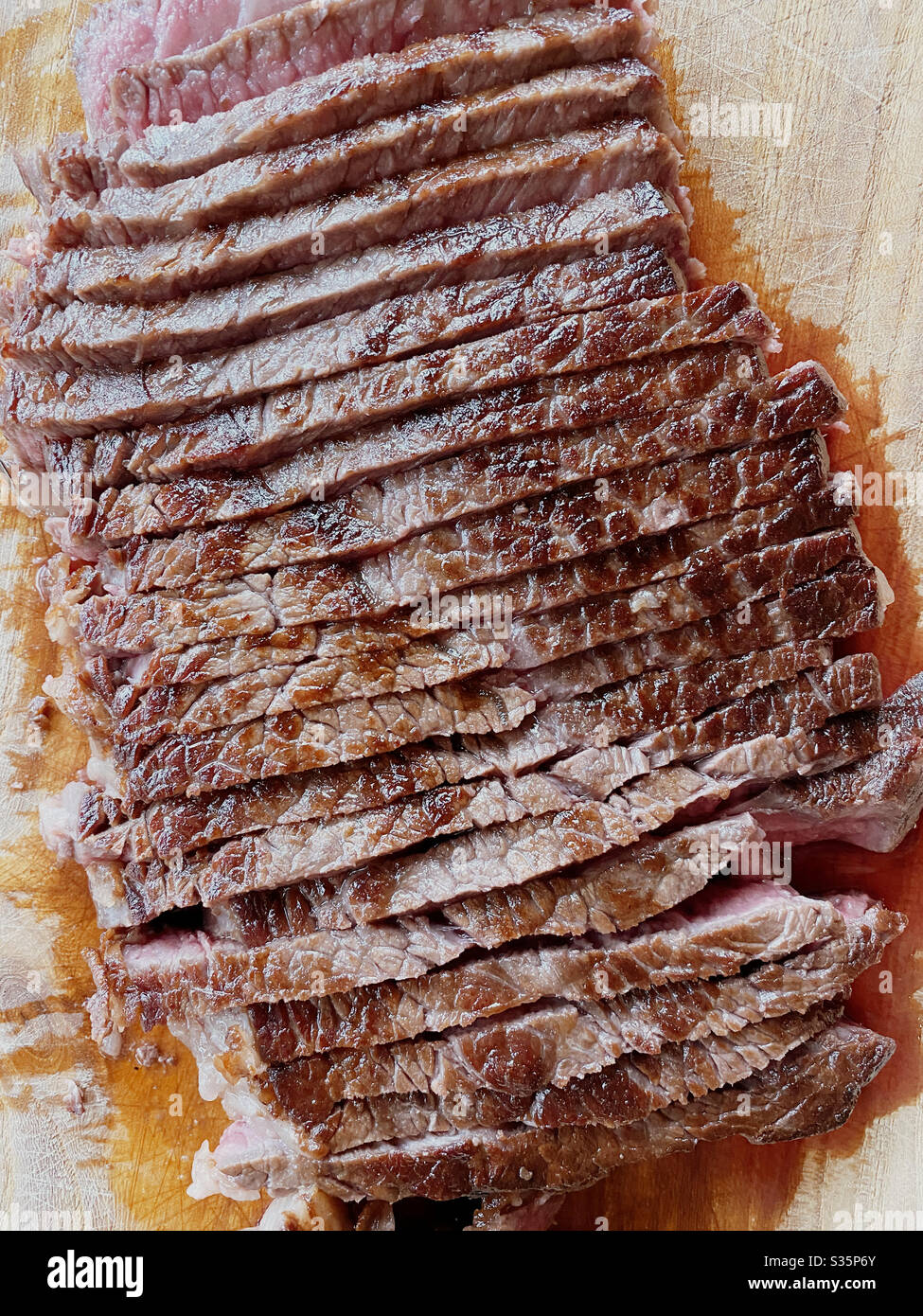 Overhead view of a shoulder steak, sliced and resting on a carving board. Stock Photo