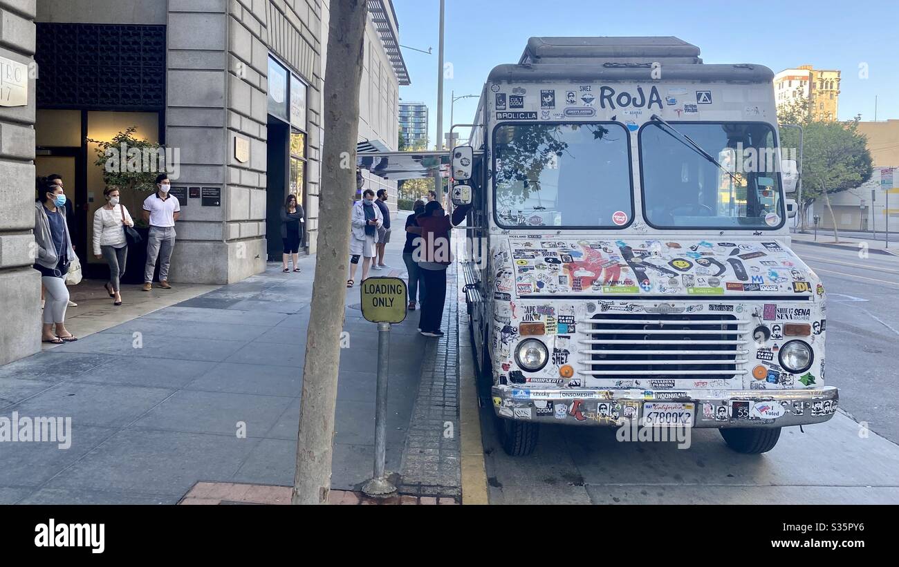 LOS ANGELES, CA, APR 2020: masked residents in Downtown wait for food at sticker-covered Kogi catering truck, parking outside apartments during Covid-19 virus lock down. Stock Photo