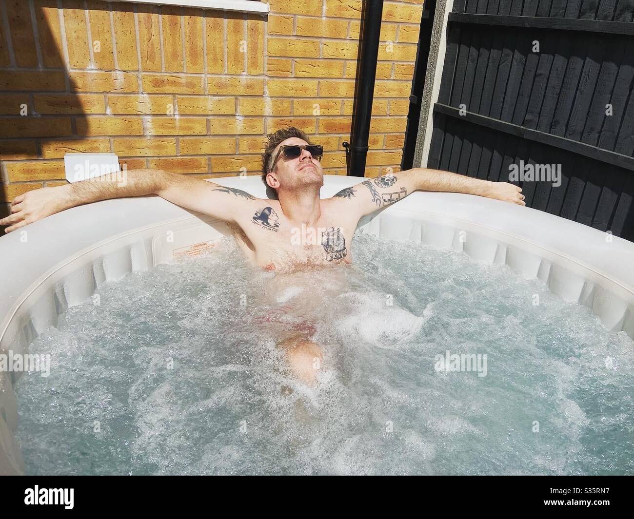 Tattooed man enjoying a soak in an inflatable hot tub - Smartphone Captured Stock Image