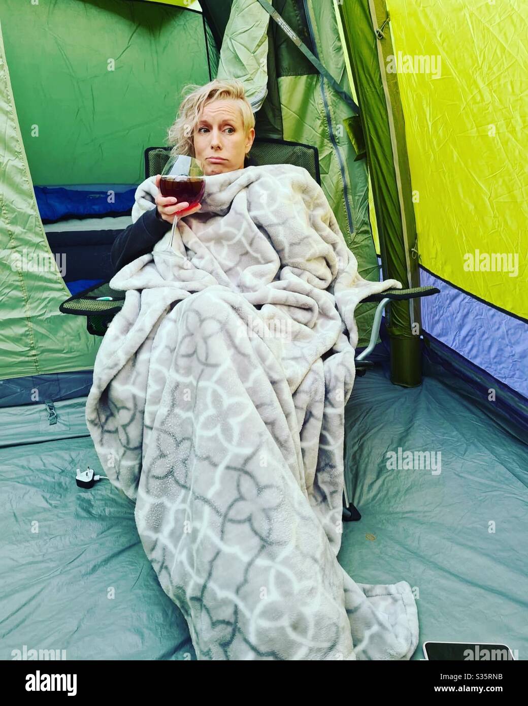 Woman drinking alcohol in a tent covered by a blanket and not looking happy - Smartphone Captured Stock Image