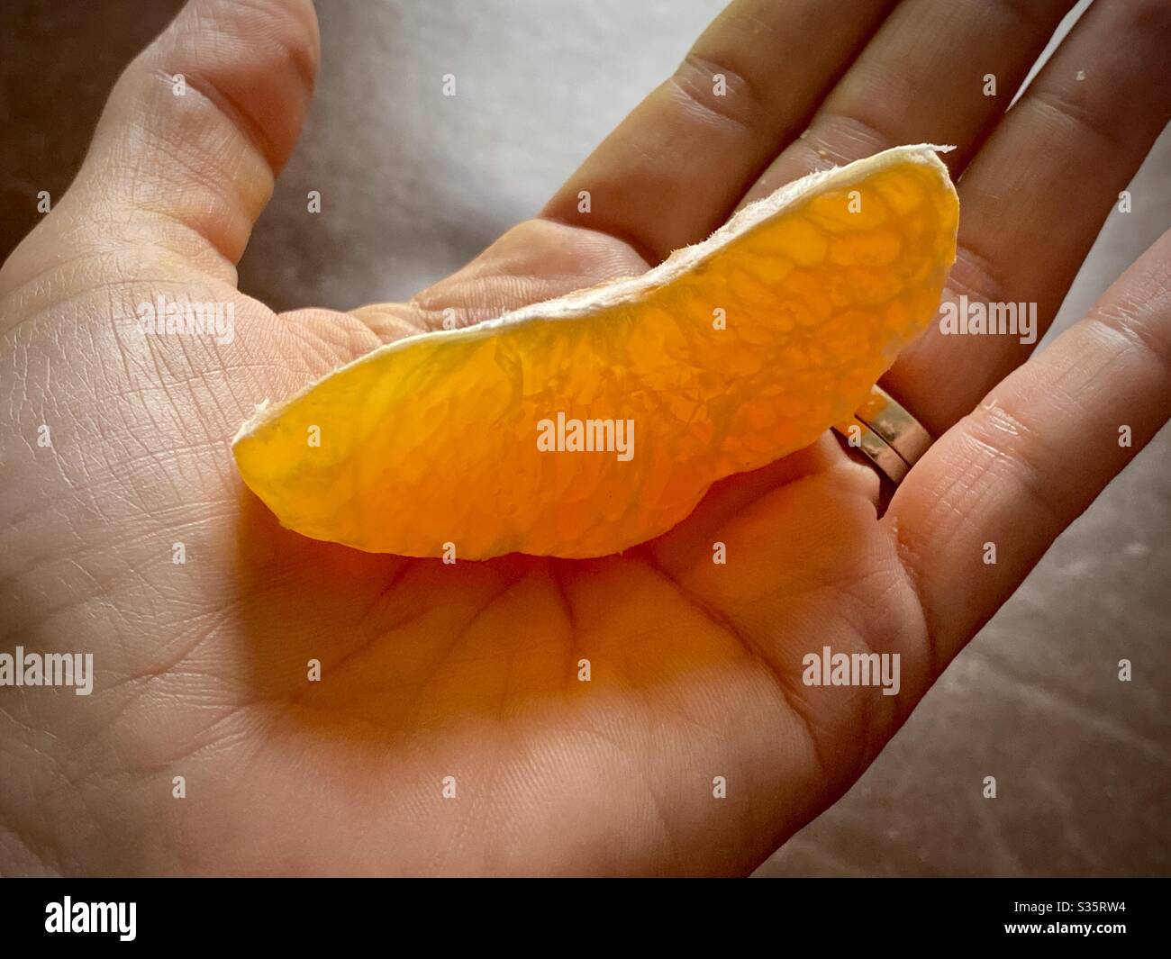 Hand holding a single segment of a peeled orange, backlit. Stock Photo