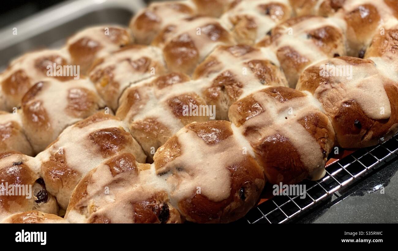 Angled view of freshly baked, fruit-filled Hot Cross Buns, cooling on a rack. Traditional Good Friday / Easter baked goods. Shallow focus Stock Photo