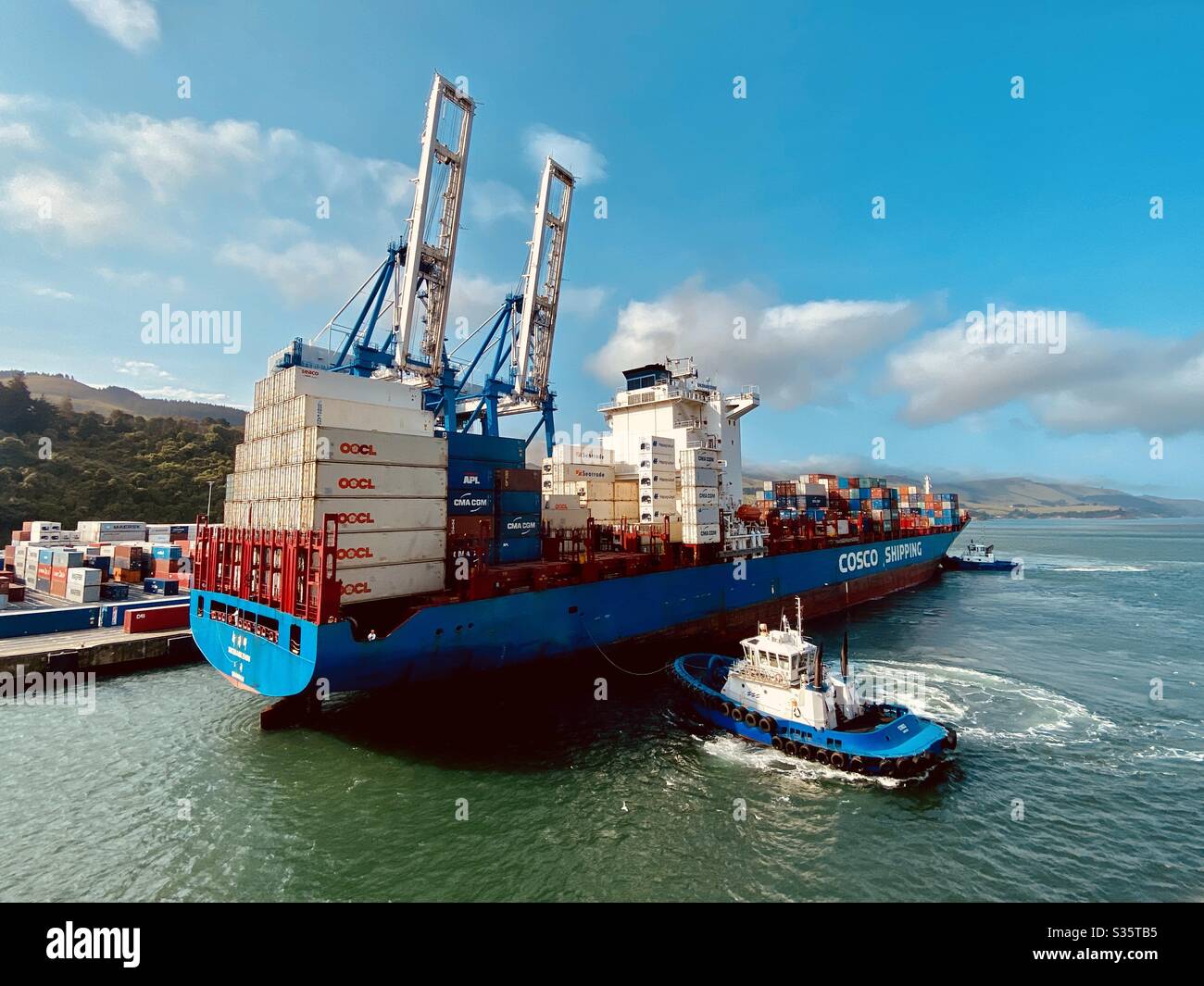 Tugs assisting the docking of a cargo freighter ship in Port Chalmers, Australia, just outside of Dunedin. Stock Photo