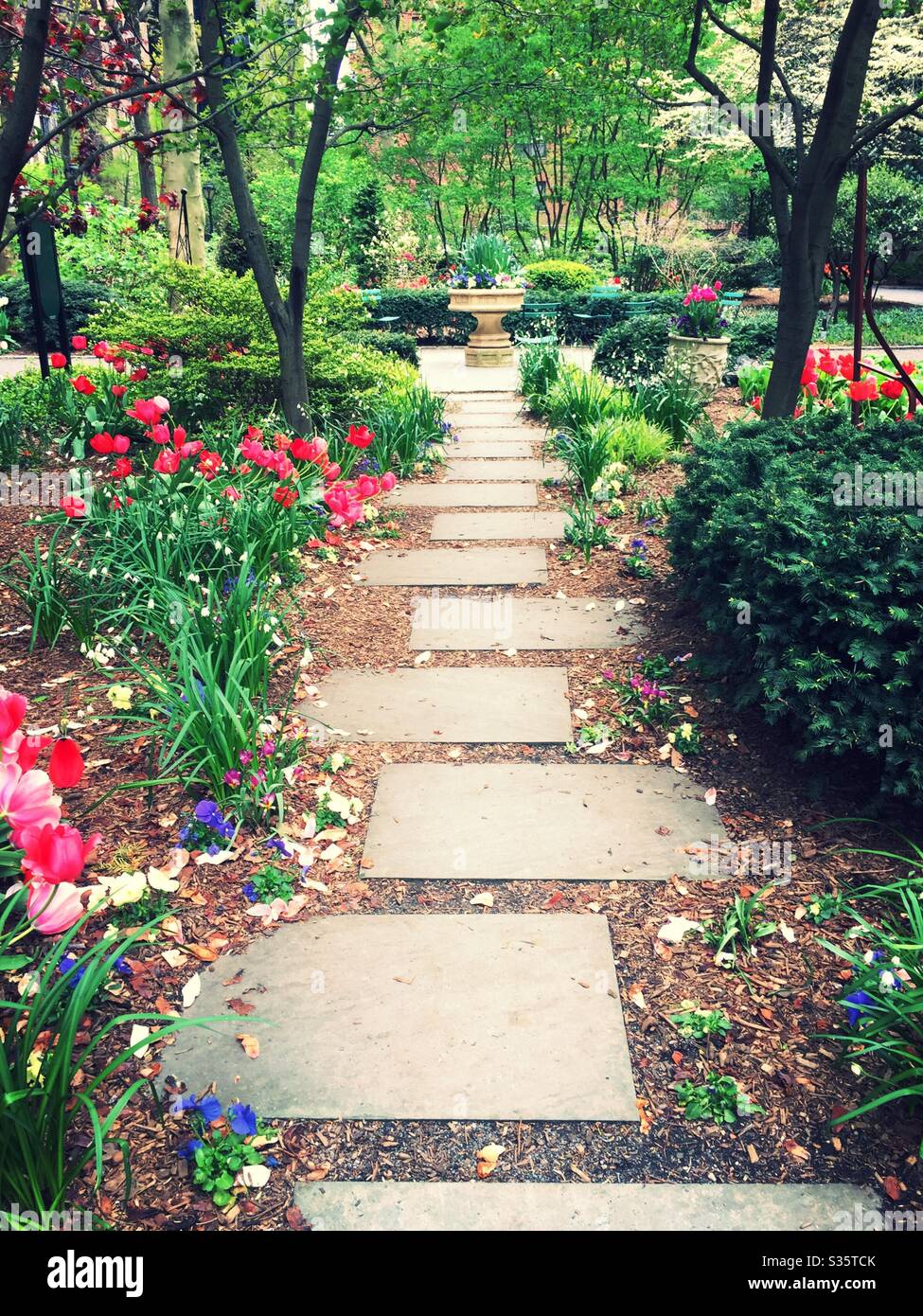 A flagstone path leads to an ornate stone birdbath in Tudor city greens, NYC, USA - Smartphone Captured Stock Image