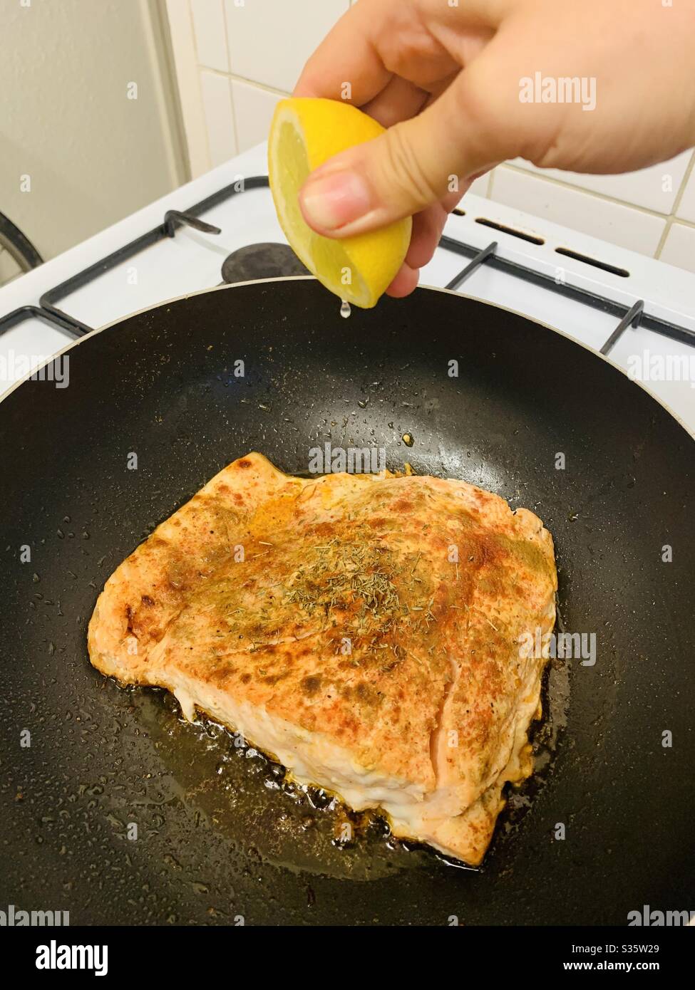 Squeezing lemon over salmon frying in a pan - Smartphone Captured Stock Image
