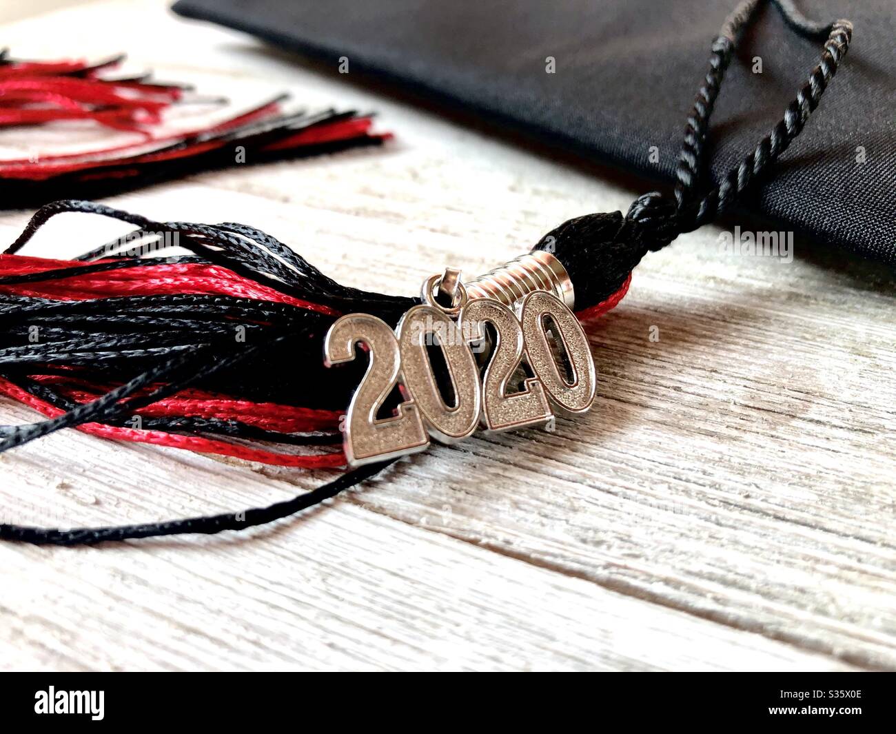 Red and black 2020 graduation cap and tassel on a wooden surface - Smartphone Captured Stock Image