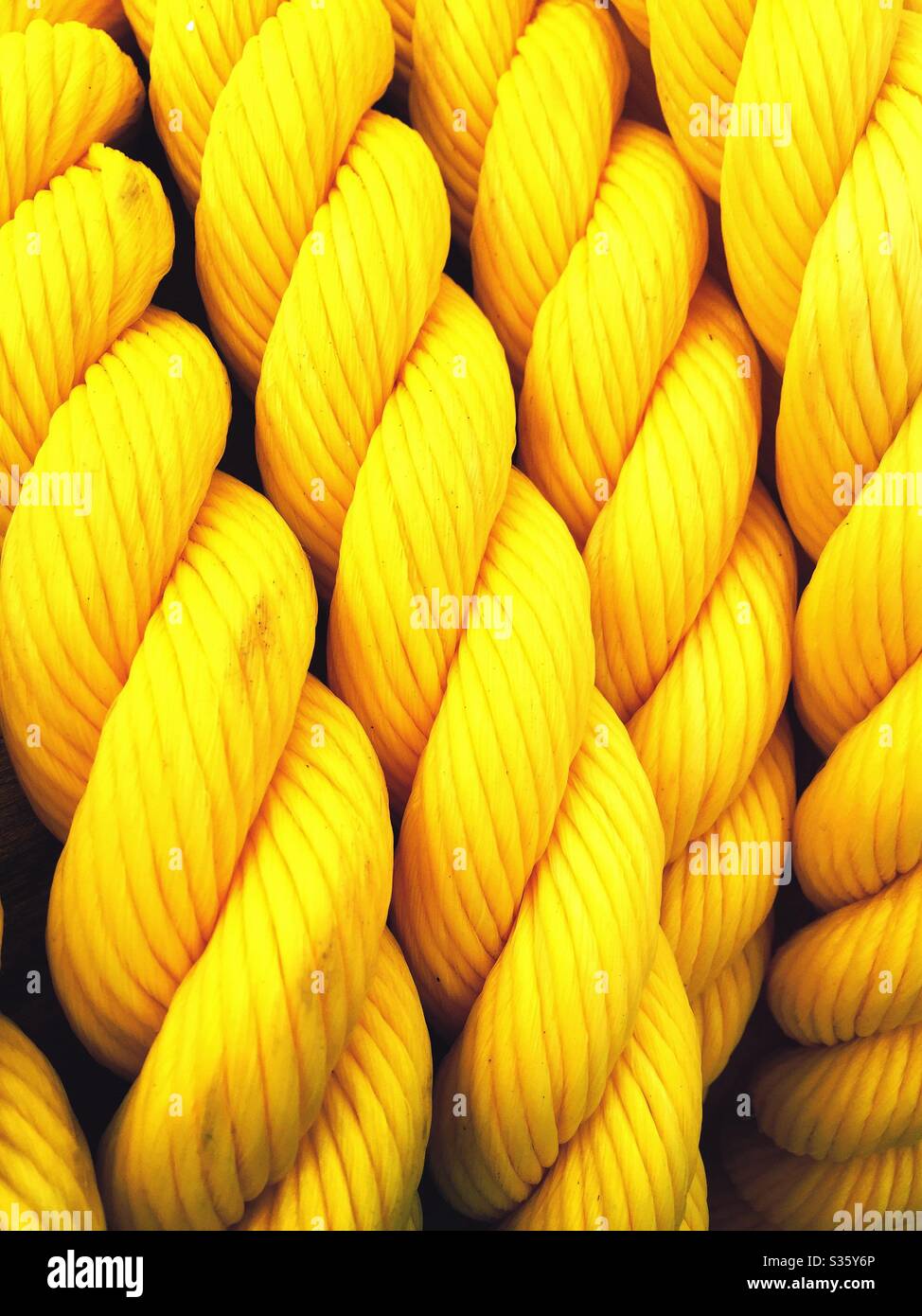 Bright yellow nylon rope. Nautical theme background. Full frame closeup detail of coiled yellow nylon rope forming patterns and shapes. Stock Photo