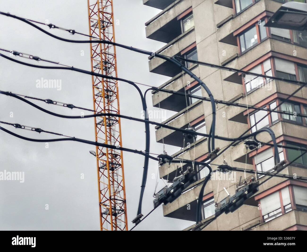Brutalist concrete building and crane viewed through trolleybus wires - Smartphone Captured Stock Image