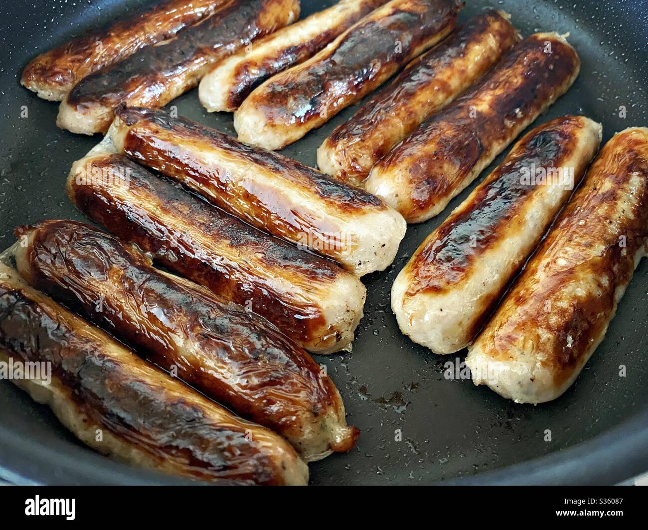 Closeup view of fresh Cumberland pork sausages sizzling in a frying pan. Fatty and tasty food. Traditional English meat breakfast in a large skillet pan. - Smartphone Captured Stock Image