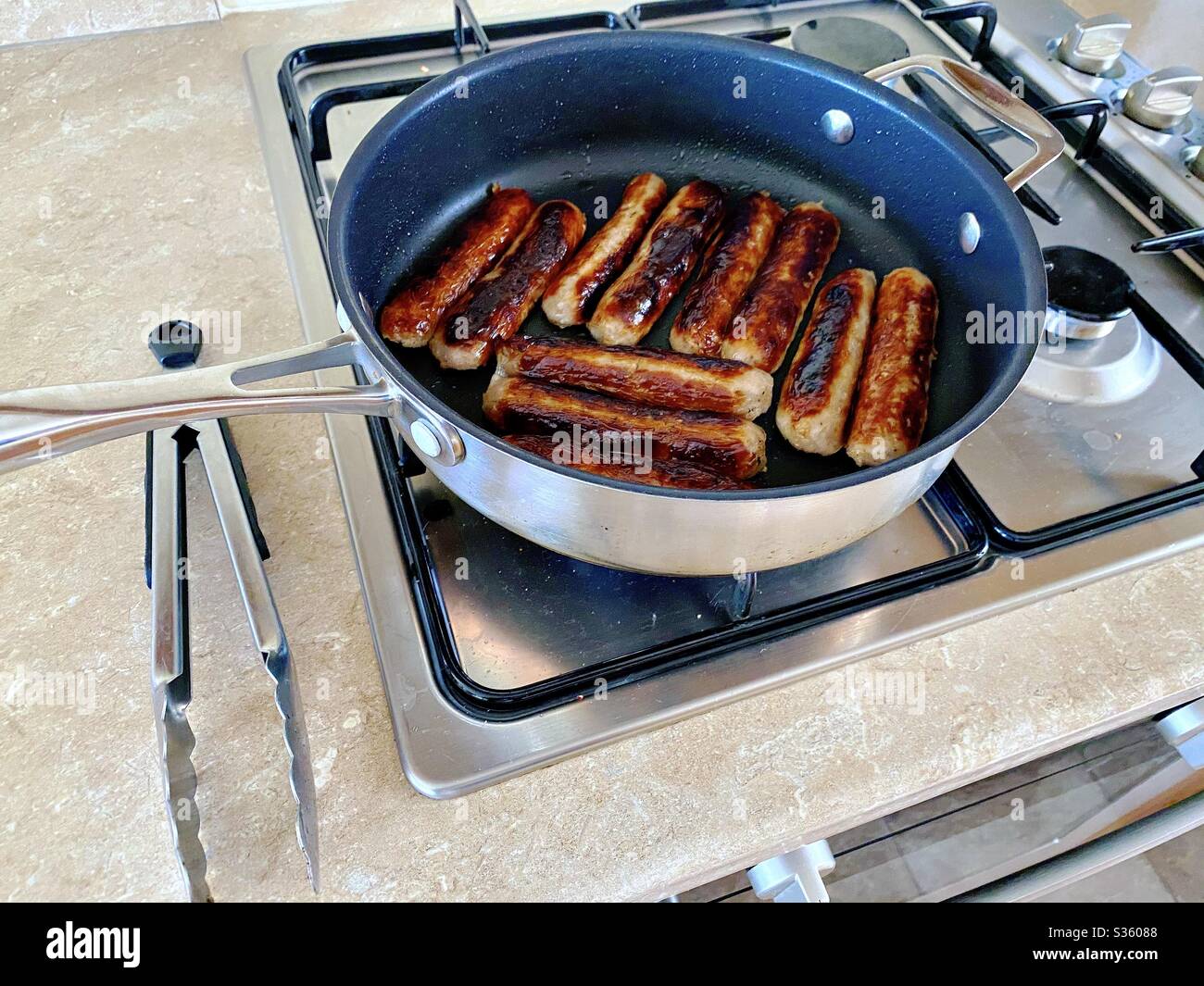 Closeup view of fresh Cumberland pork sausages sizzling in a frying pan. Fatty and tasty food. Traditional English meat breakfast in a large skillet pan. - Smartphone Captured Stock Image