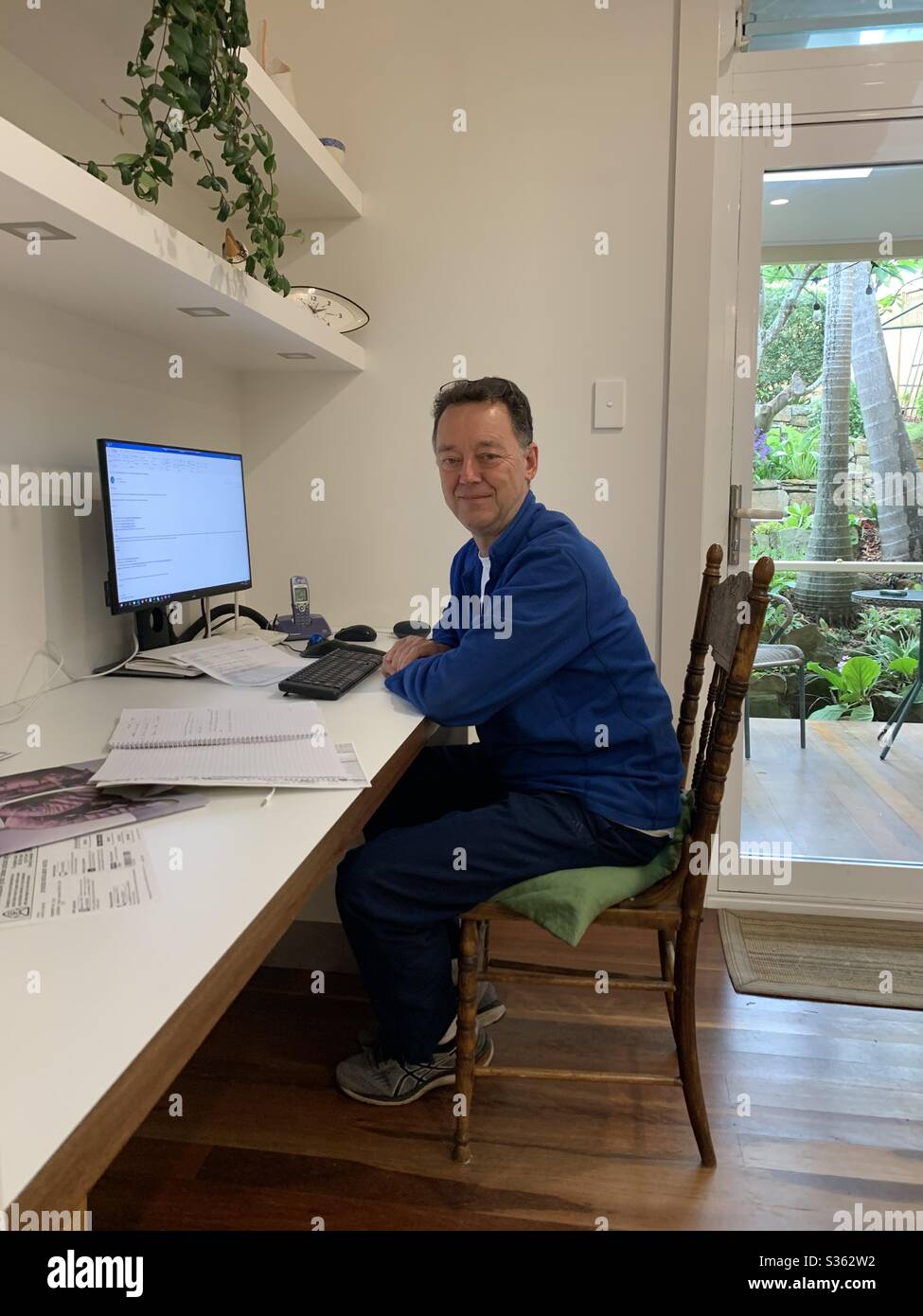 A white Australian adult male person sits at a modern home workstation during the pandemic and works from home - Smartphone Captured Stock Image
