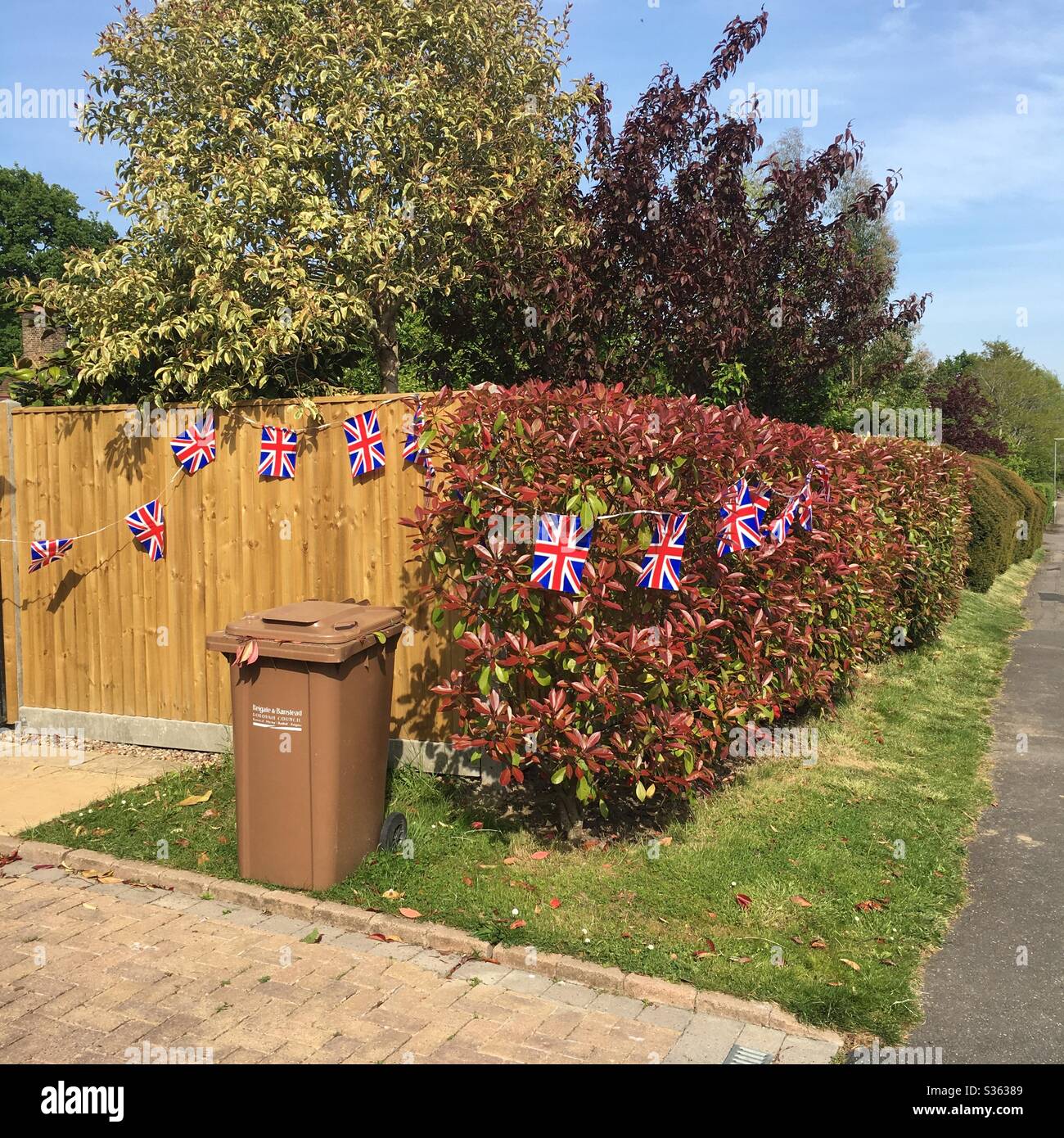 VE Day on bin day - VE Day celebrations with a hedge and fence decorated with Union Jack flag bunting Stock Photo