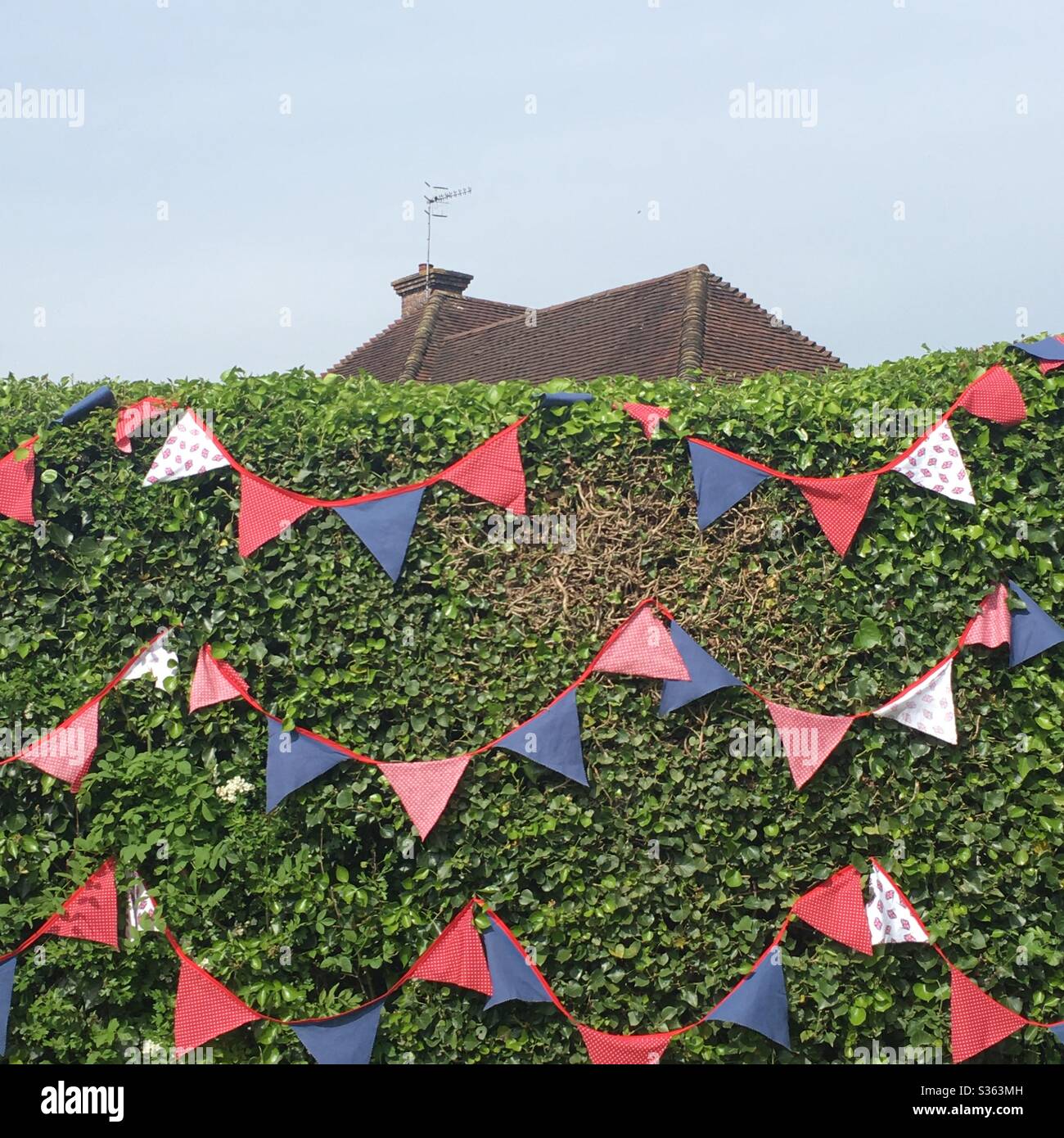VE Day bunting celebrations on a hedge during lockdown 8th May 2020 Surrey England UK - Smartphone Captured Stock Image