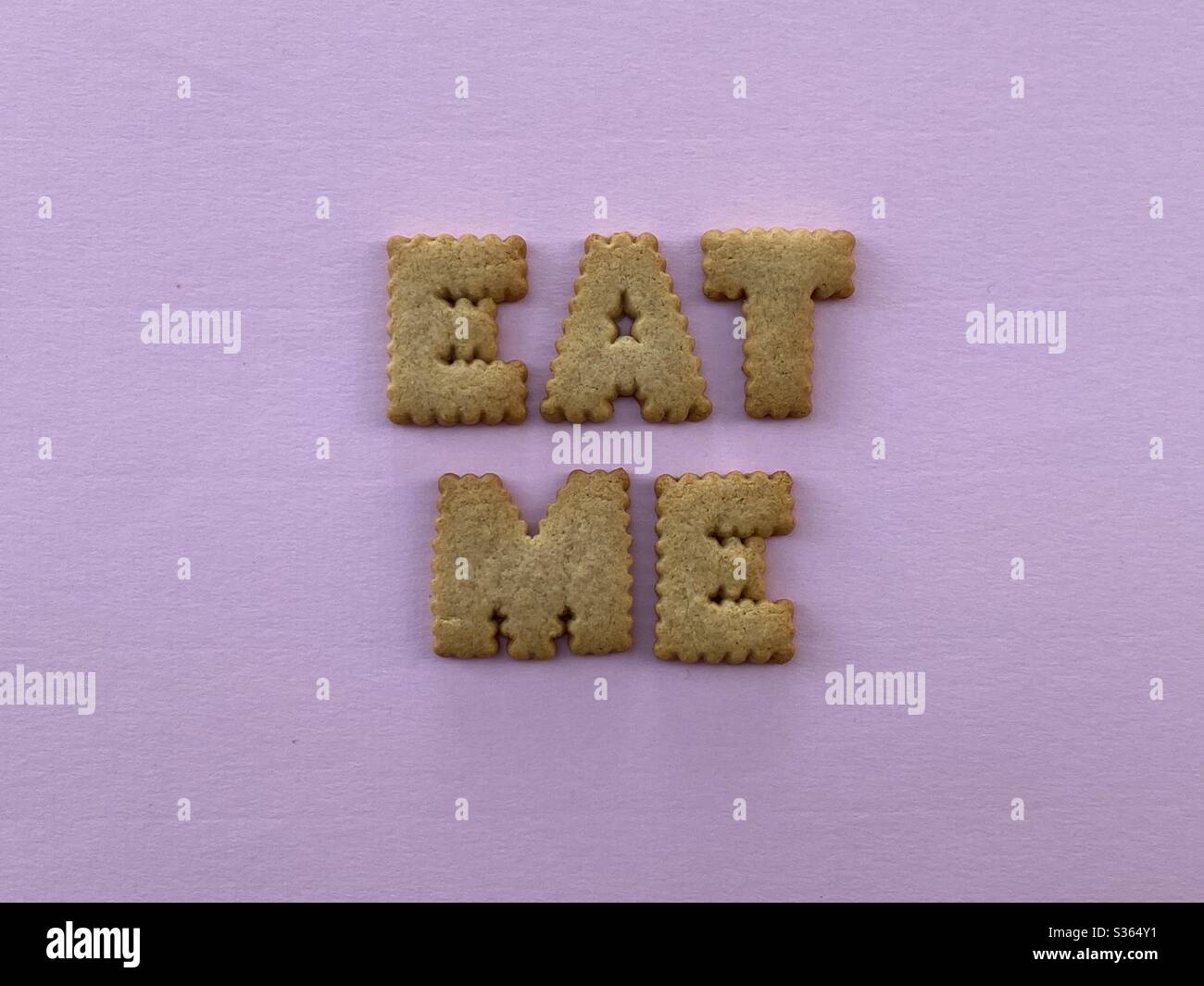 Eat me, creative text composed with biscuit letters on pink background - Smartphone Captured Stock Image