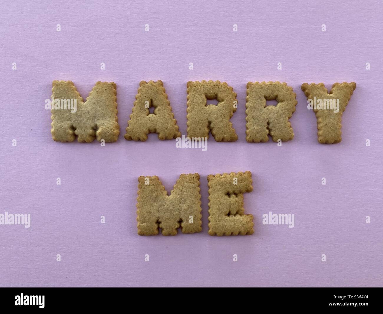 Marry me message composed with biscuit letters over pink background - Smartphone Captured Stock Image