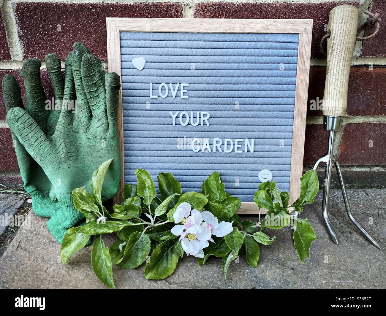 Love your garden. Gardening concept with felt letter board, handheld prune, dirty gloves and a pruned branch with blossom from an apple tree on a stone patio - Smartphone Captured Stock Image