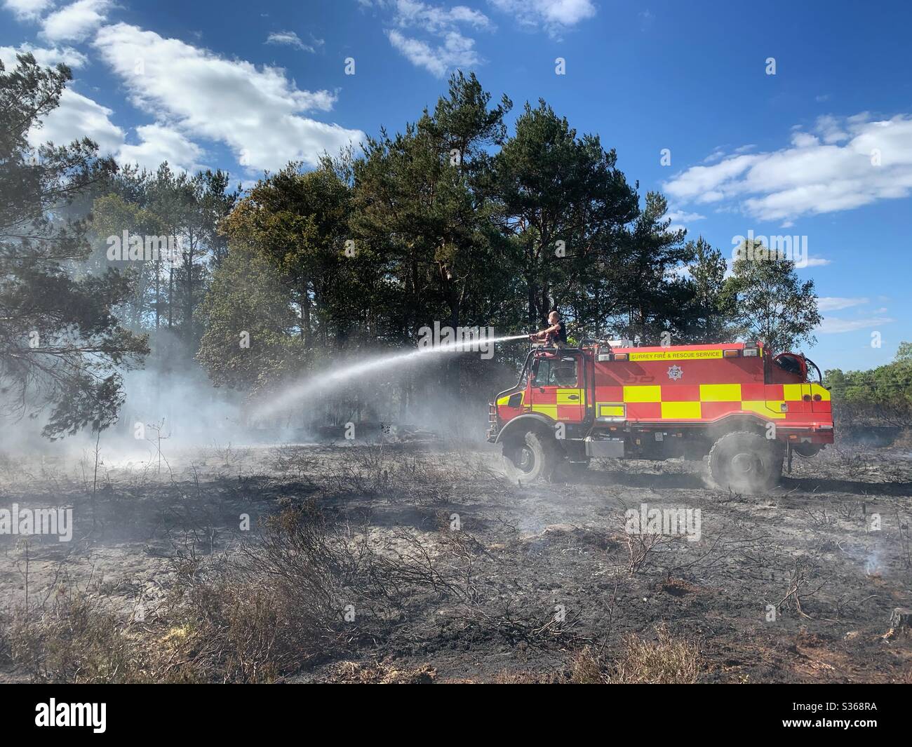 An off-road firefighting vehicle sprays water during a wildfire on heathland in Hampshire. Stock Photo