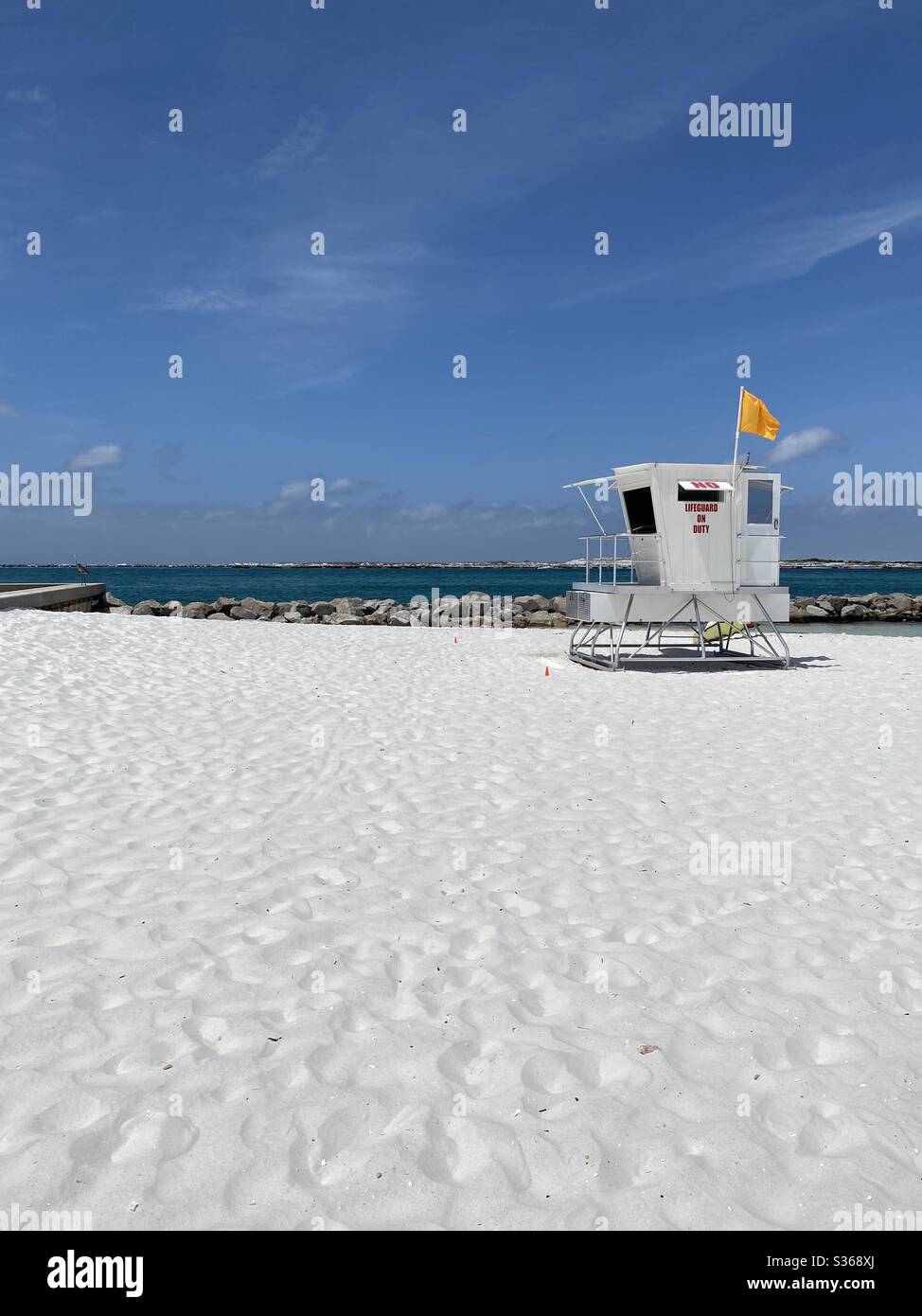 Lifeguard stand on public white sand beach with yellow flag flying - Smartphone Captured Stock Image