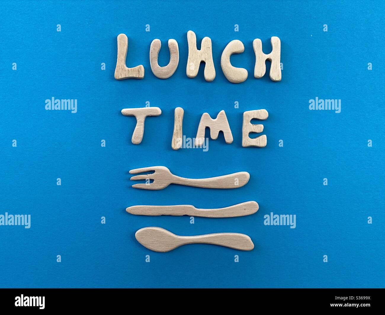 Lunch time text composed with wooden artistic letters with wooden fork, knife and spoon design over blue background Stock Photo