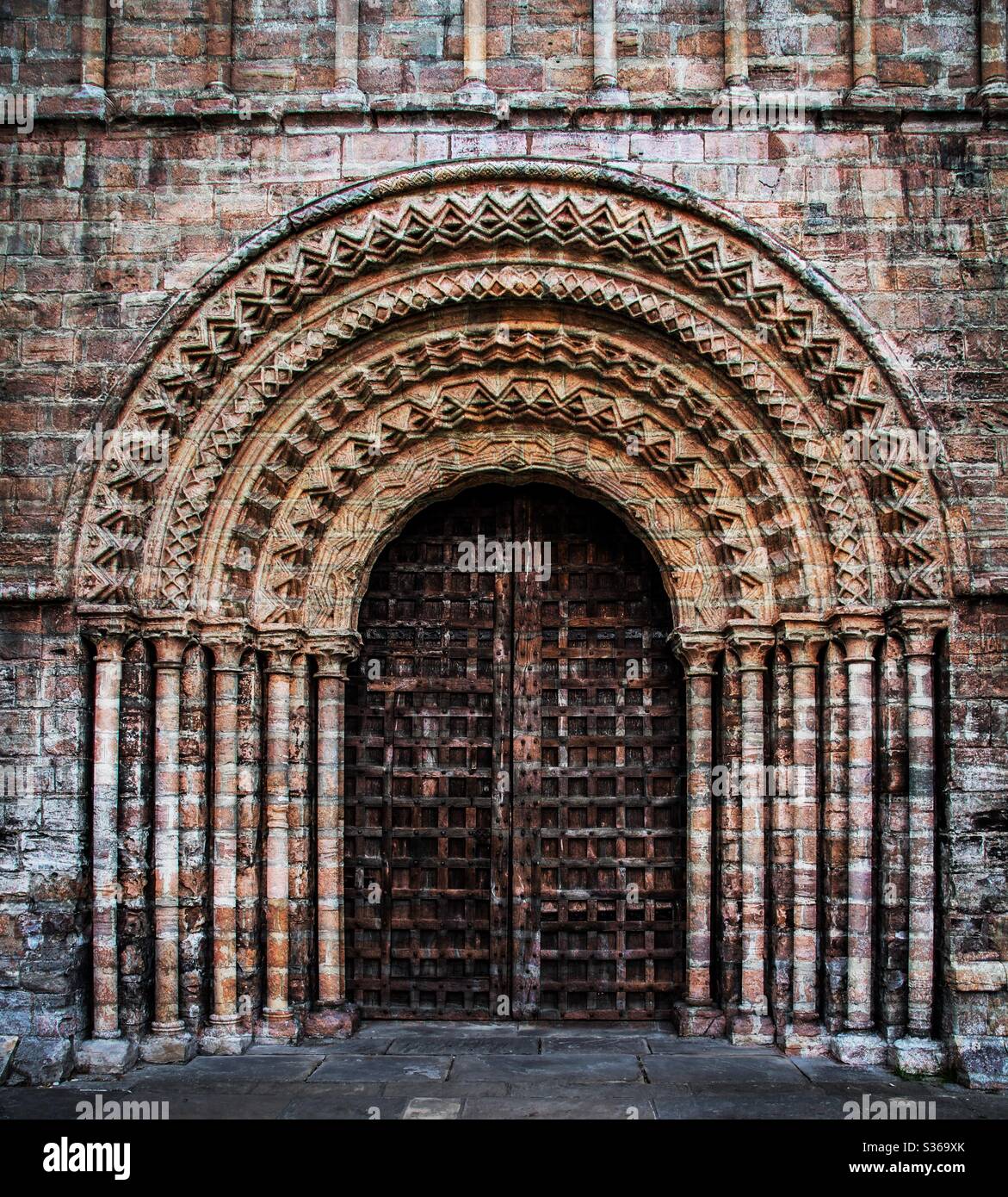 A Gothic and ornate church door with intricate, carved stone arches and pillars with a heavy, solid wooden door - Smartphone Captured Stock Image