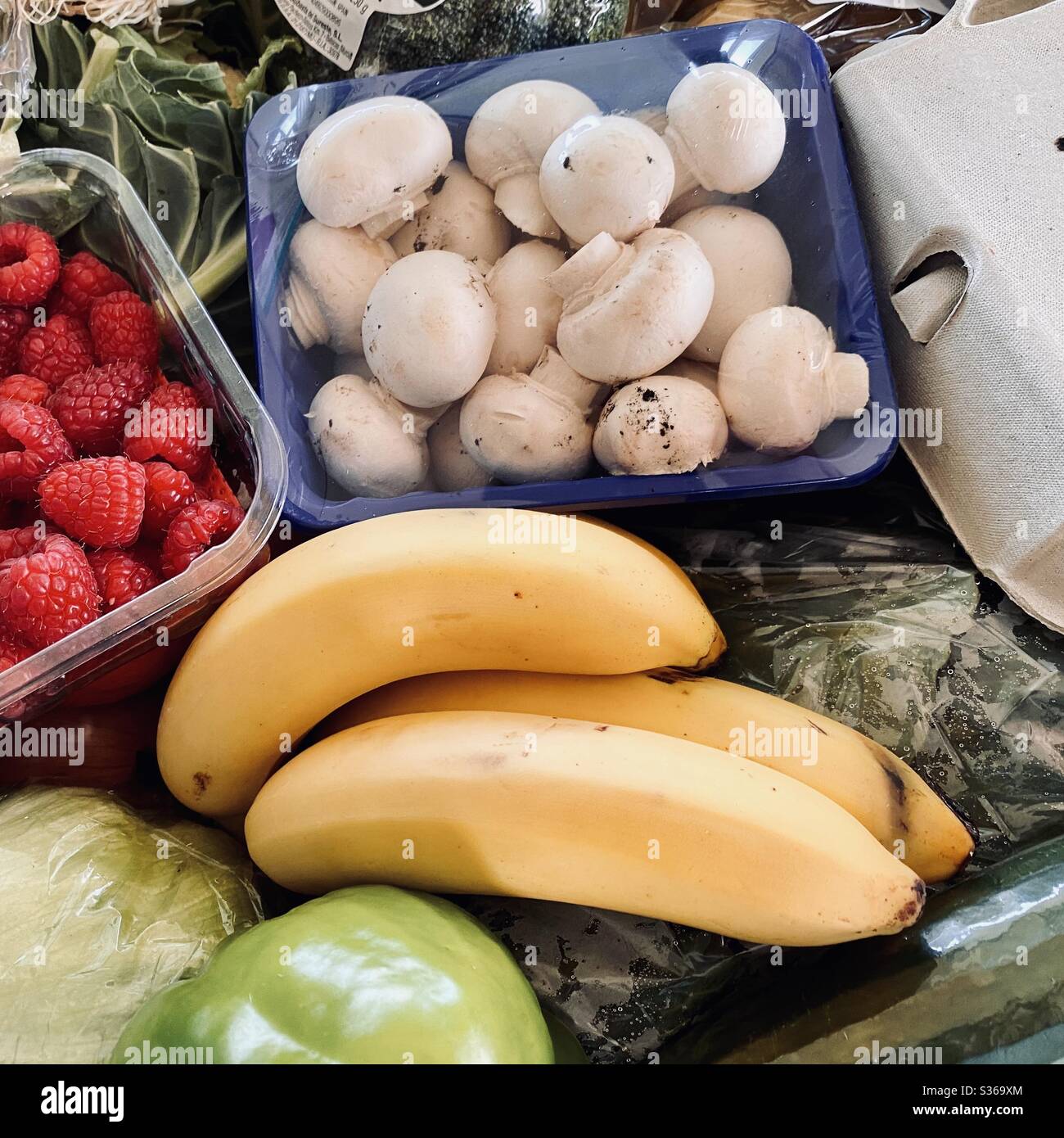 Close up view of fresh fruit and vegetables filling the frame with healthy color. Raspberries, bananas, mushrooms and salad greens in a crate of mixed fruit and veg. - Smartphone Captured Stock Image