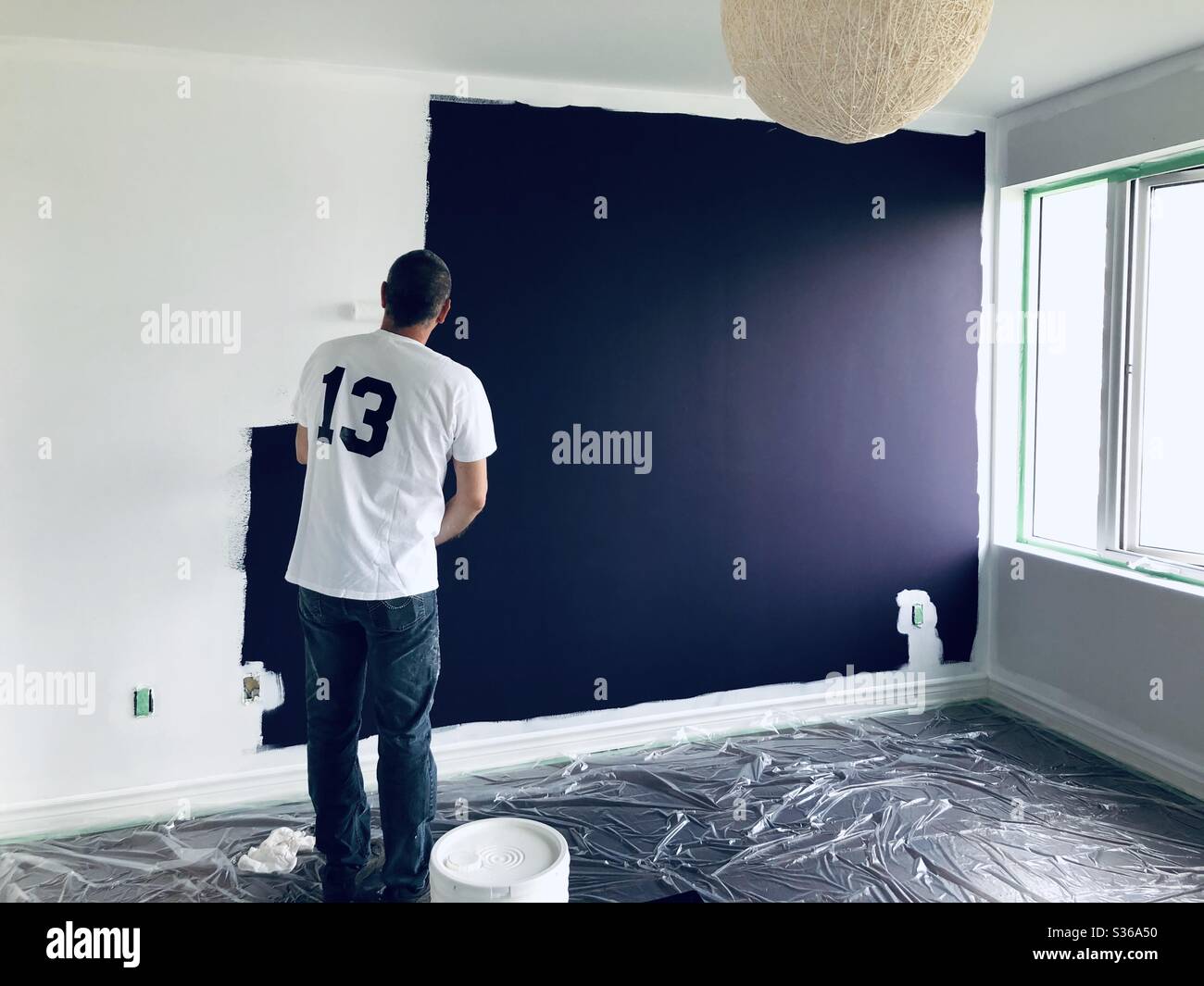 Man painting the walls white over purple color - Smartphone Captured Stock Image