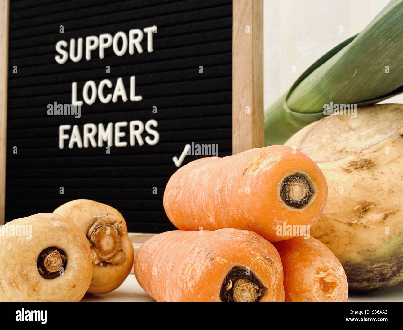 A selective focus view of a blurry farmer’s market sign behind fresh produce. Support local farmers. Fresh carrots, parsnips. Locally sourced, organic & healthy veggies. Supporting local business. - Smartphone Captured Stock Image