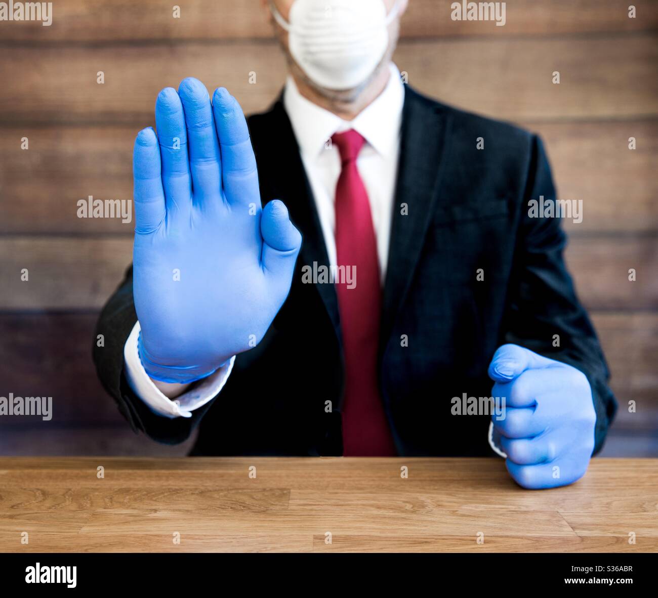 A Coronavirus doctor or businessman wearing ppe including blue, surgical gloves and face mask holding his Hand up in a stop gesture to keep people social distancing and self isolating - Smartphone Captured Stock Image