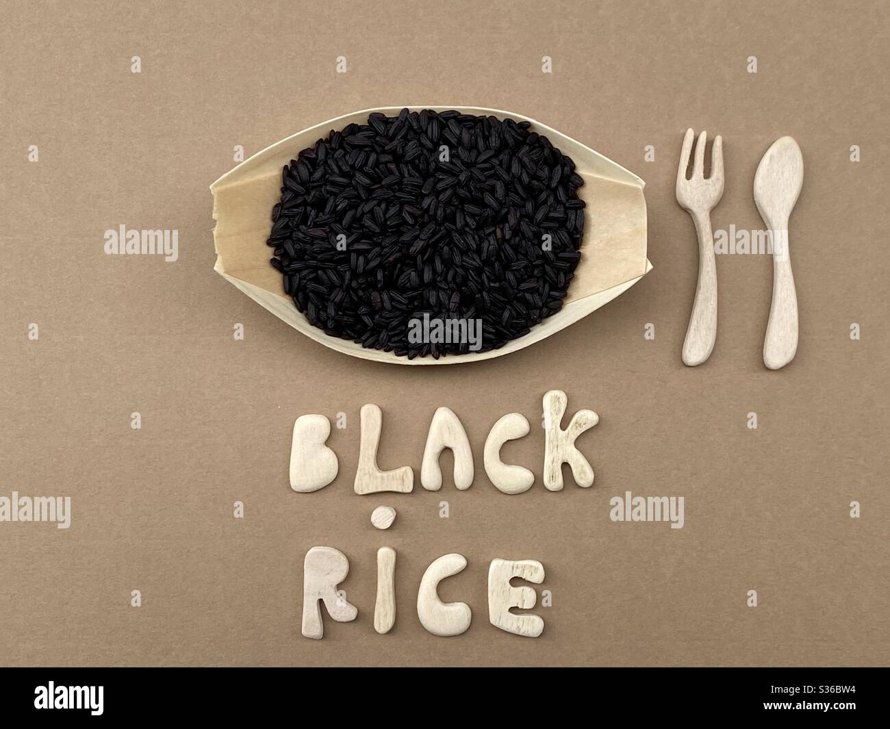 Black rice composed with handmade wooden letters and cutlery - Smartphone Captured Stock Image
