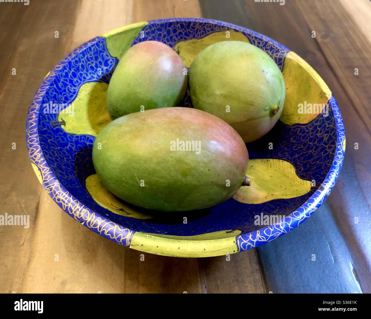 Still life of 3 different sized mangos in a colorfully painted wooden bowl. Stock Photo