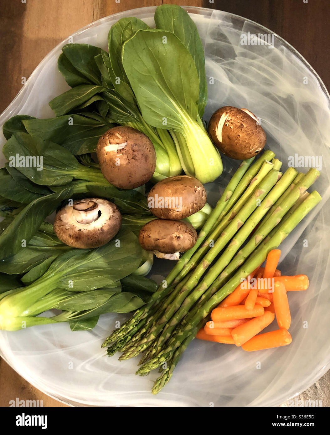 Still life of fresh vegetables consisting of baby bok choy, portobello mushrooms, asparagus and baby carrots in a white recycled-glass bowl. - Smartphone Captured Stock Image
