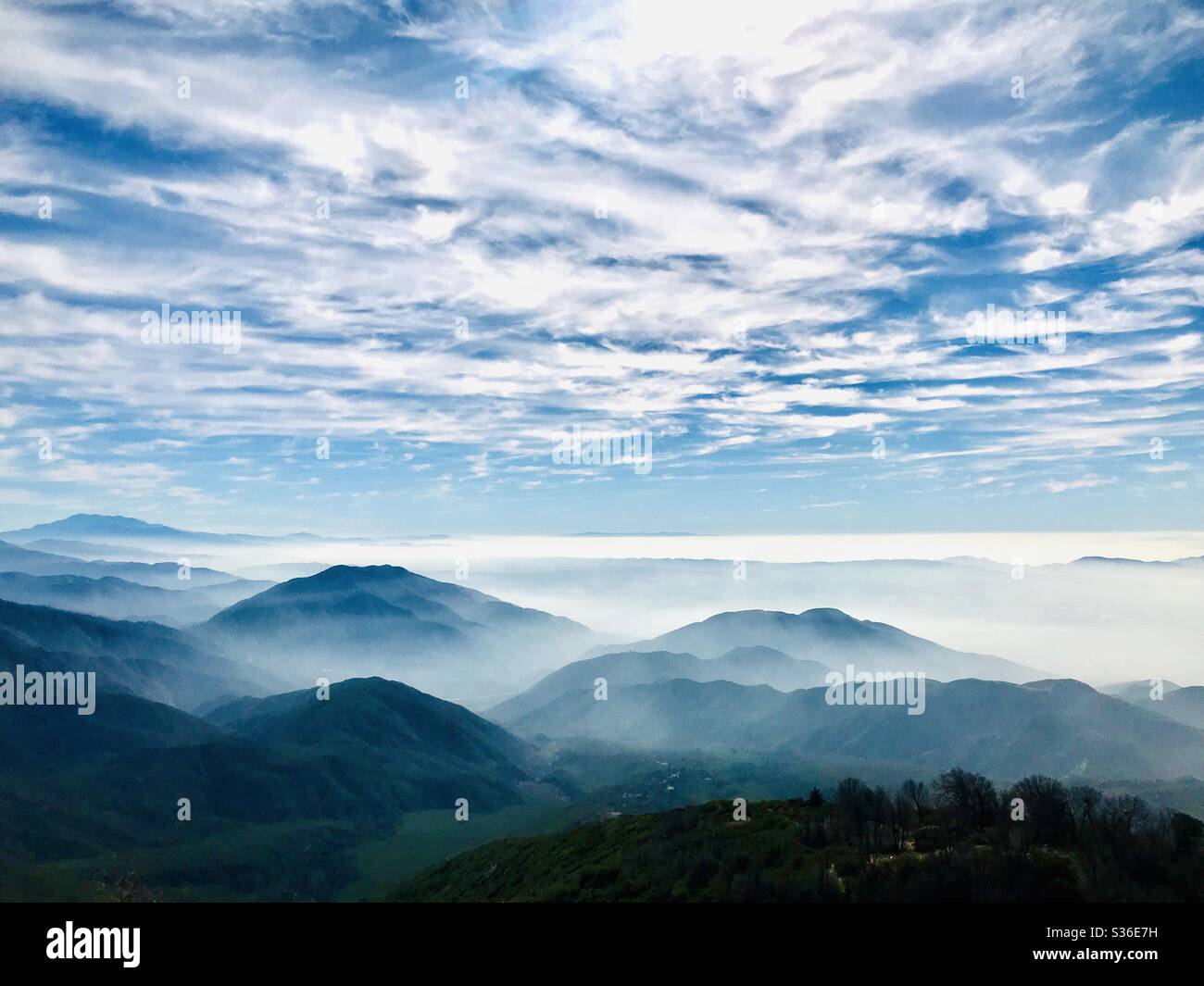 A cloud filled blue sky looms over layers of mountains. Stock Photo