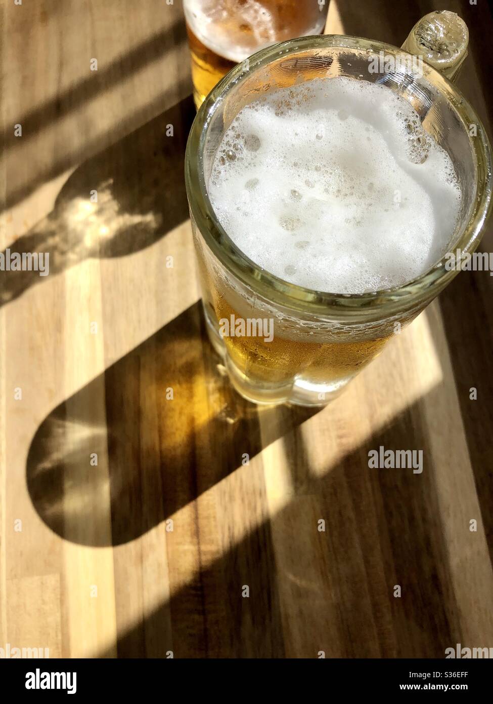 Glass mug of beer on a wood surface with sunlight shining through Stock Photo