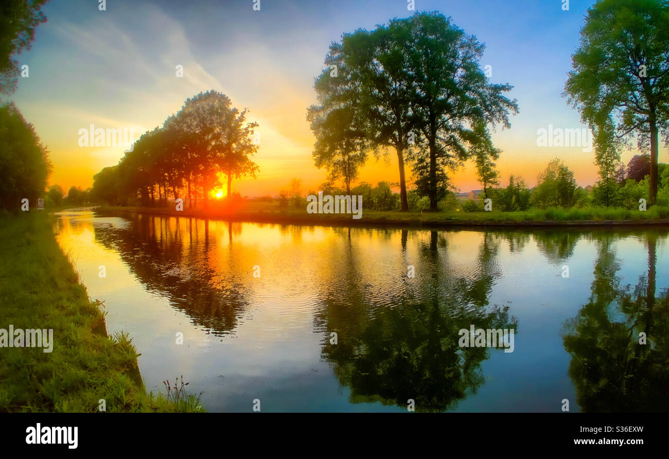 Glowing orange red sunset reflected in the water of the river Stock Photo